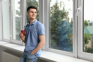 Photo of Handsome young man with glass of juice near window at home