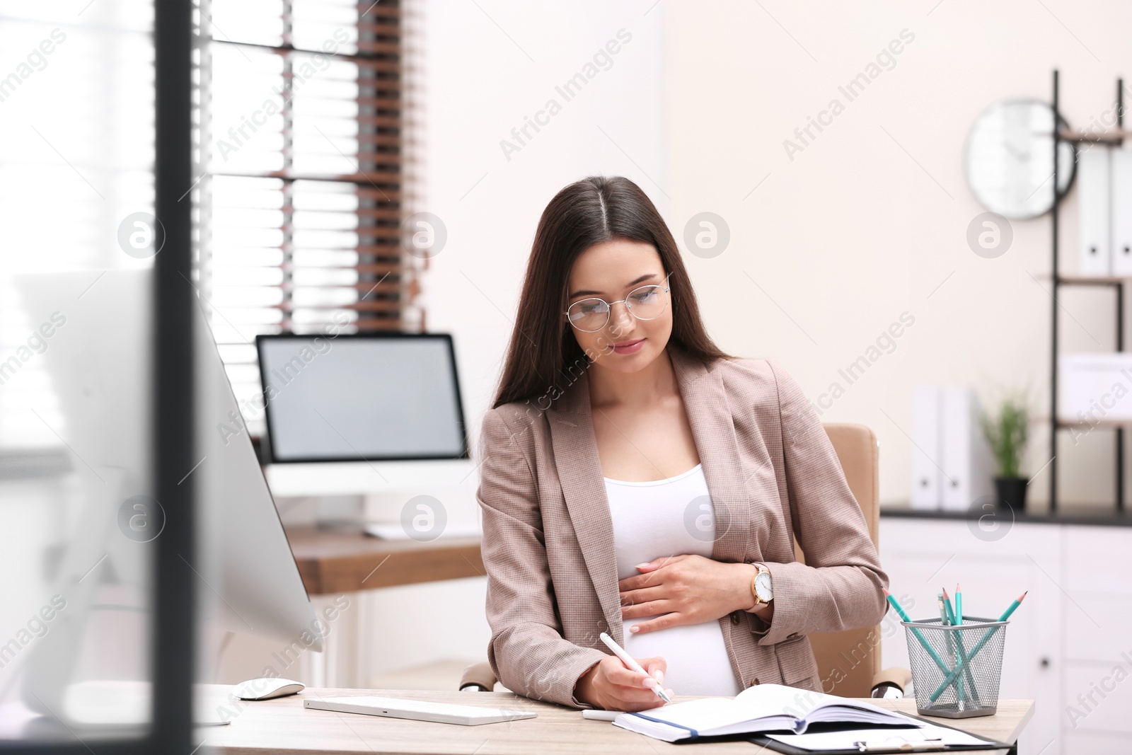 Photo of Young pregnant woman working at desk in office