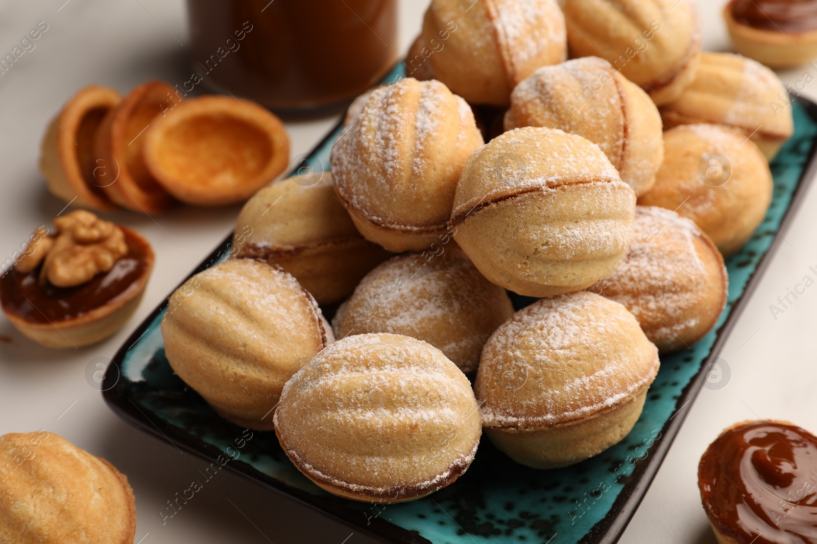 Photo of Homemade walnut shaped cookies with boiled condensed milk on white marble table, closeup