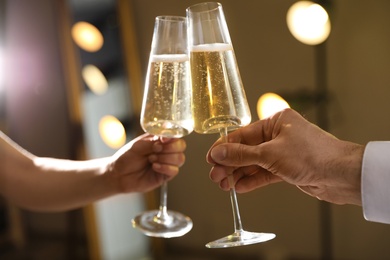 Photo of Man and woman clinking glasses of champagne on blurred background, closeup