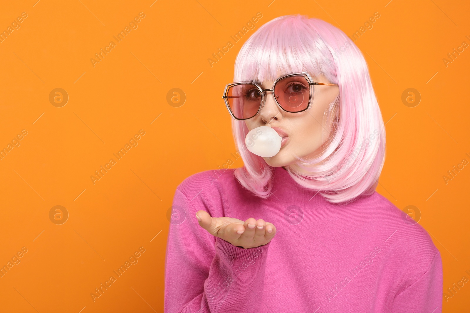 Photo of Beautiful woman in sunglasses blowing bubble gum on orange background