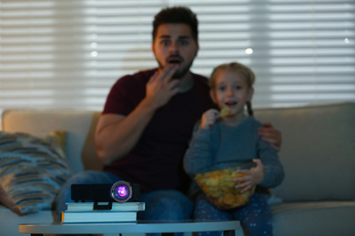 Young man and his daughter watching movie at home, focus on video projector