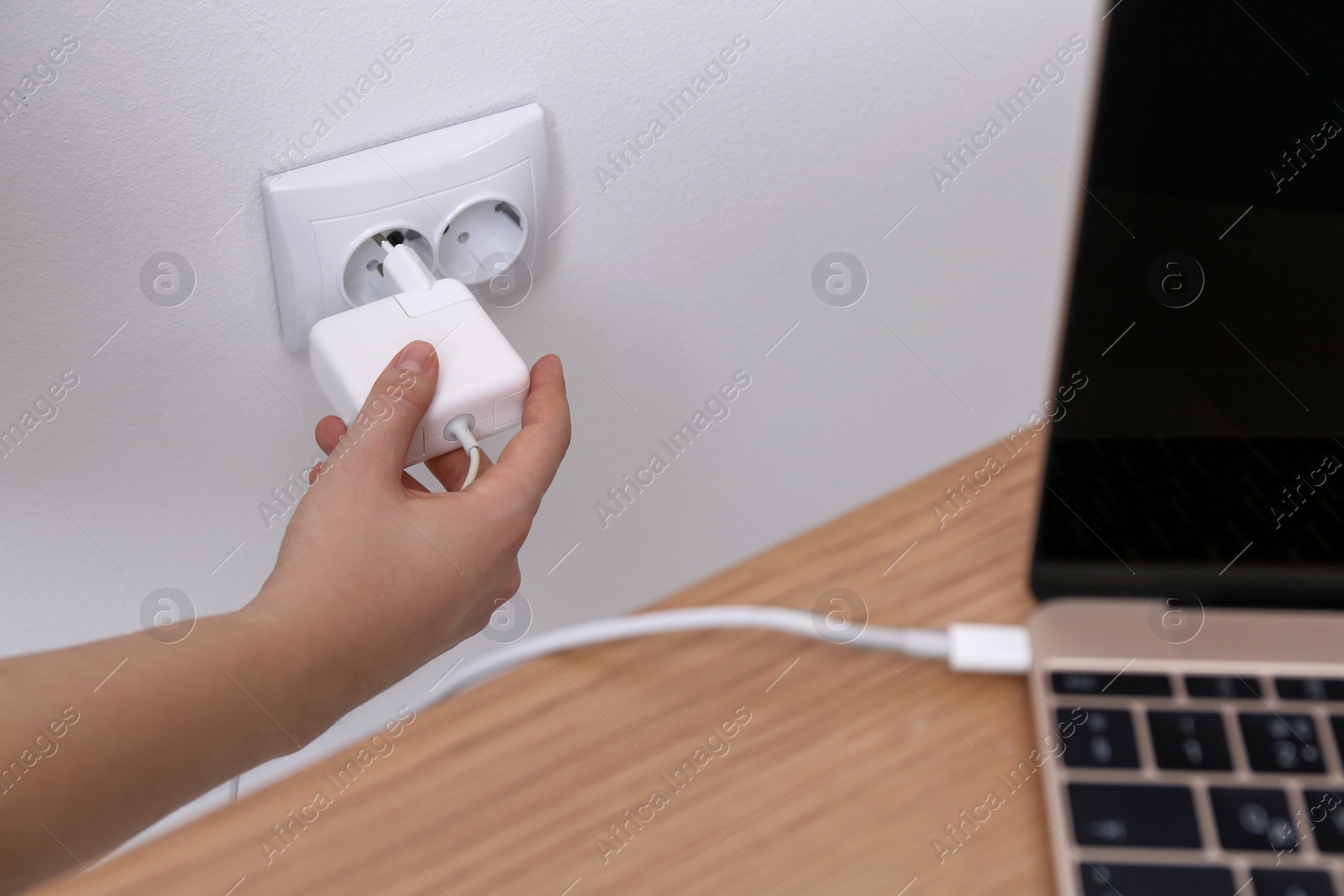 Photo of Woman inserting power plug for laptop charging into wall socket indoors, closeup