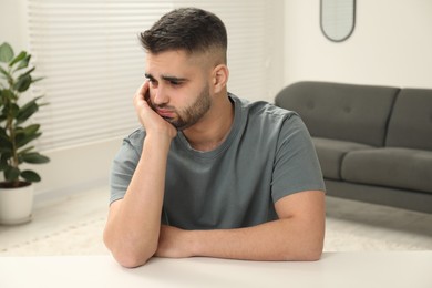 Sad man sitting at white table indoors