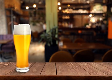 Image of Glass with cold tasty beer on wooden table in pub, space for text