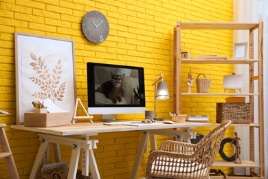Stylish home office interior with comfortable workplace near yellow brick wall