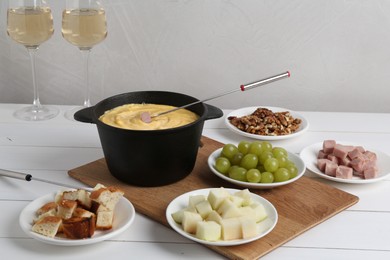 Photo of Fondue pot with tasty melted cheese, forks, wine and different snacks on white wooden table