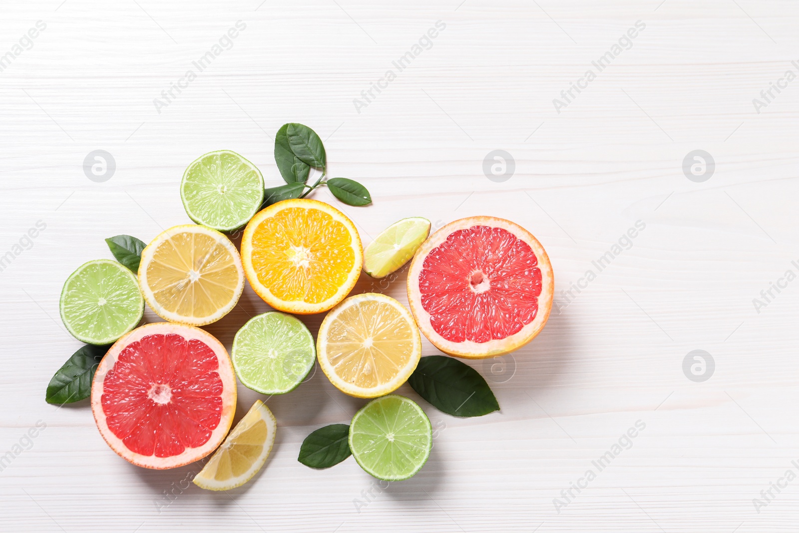 Photo of Different cut citrus fruits and leaves on white wooden table, flat lay. Space for text