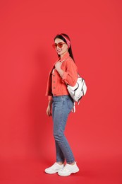 Beautiful young woman with stylish leather backpack on red background