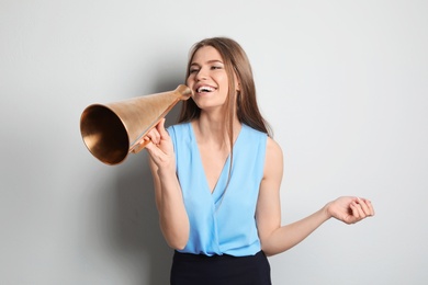 Photo of Young woman using megaphone on light background