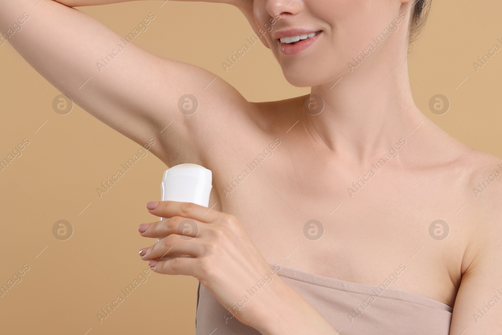 Photo of Woman applying deodorant on beige background, closeup