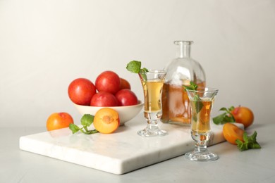 Photo of Delicious plum liquor with mint and ripe fruits on light table. Homemade strong alcoholic beverage