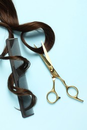 Professional hairdresser scissors and comb with brown hair strand on light blue background, flat lay