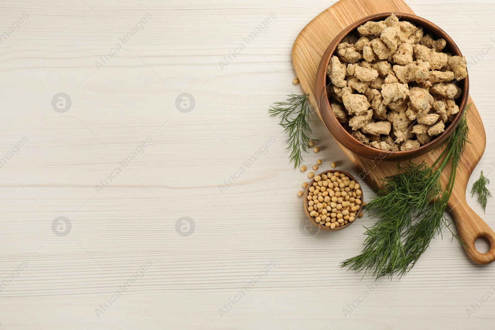 Photo of Dried soy meat in bowl on white wooden table, flat lay. Space for text