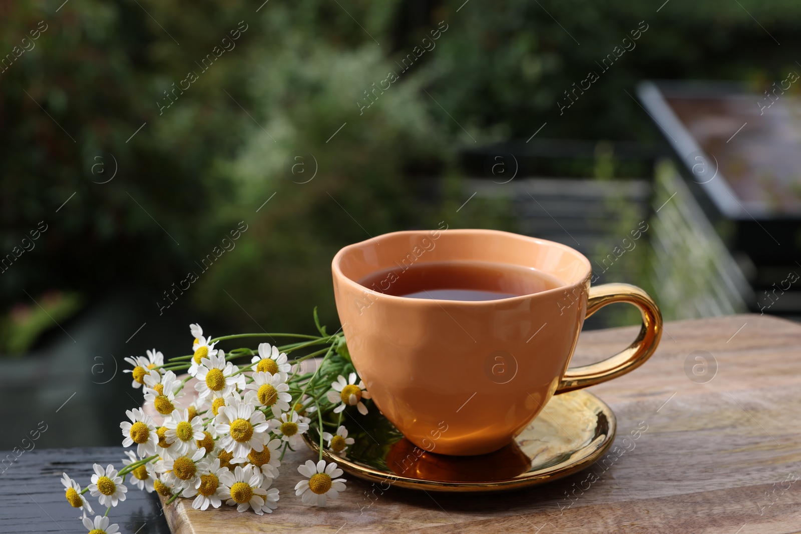 Photo of Cup of delicious chamomile tea and fresh flowers outdoors