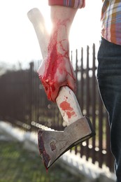 Photo of Man holding bloody axe outdoors, closeup view