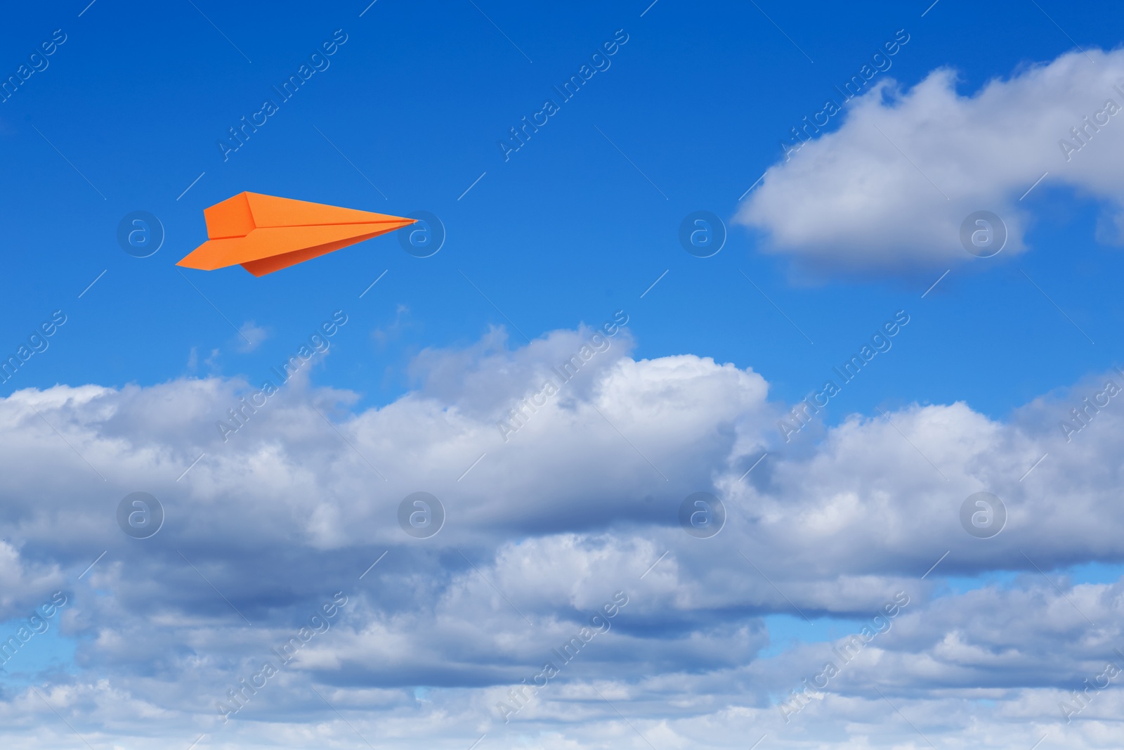 Image of Orange paper plane flying in blue sky with clouds