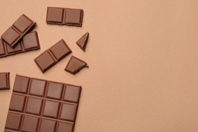 Pieces of delicious chocolate bar on beige background, flat lay. Space for text