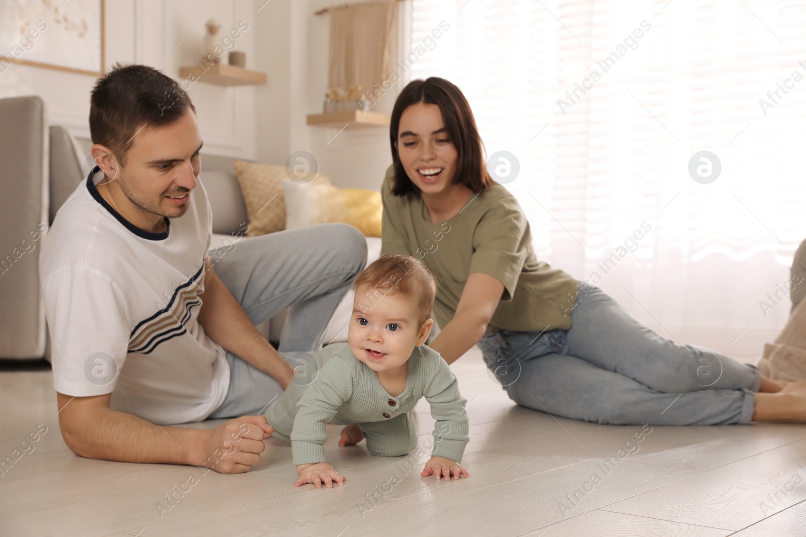 Photo of Happy parents helping their baby to crawl on floor at home