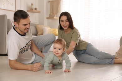 Happy parents helping their baby to crawl on floor at home