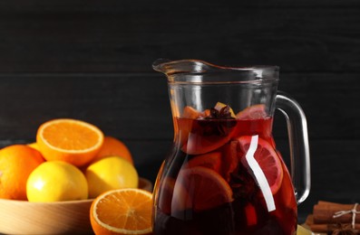 Glass jug of aromatic punch drink and ingredients on table, closeup. Space for text