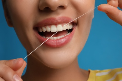 Young woman flossing her teeth on blue background, closeup. Cosmetic dentistry