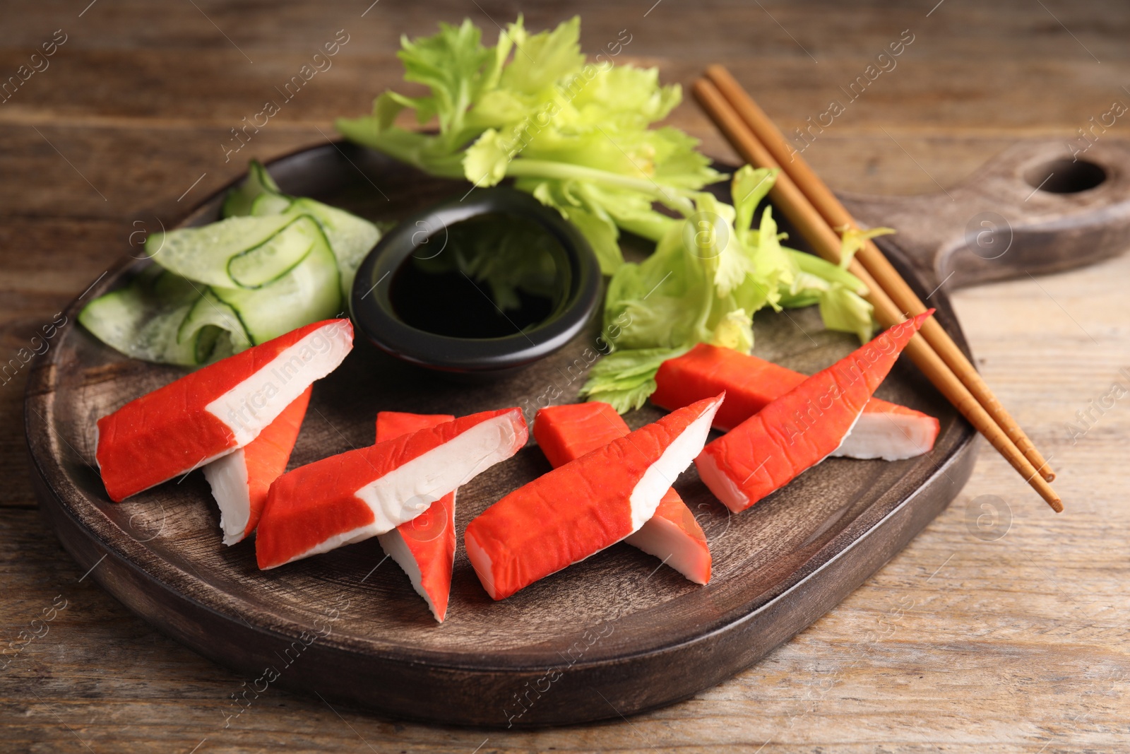 Photo of Fresh crab sticks with lettuce and soy sauce served on wooden table