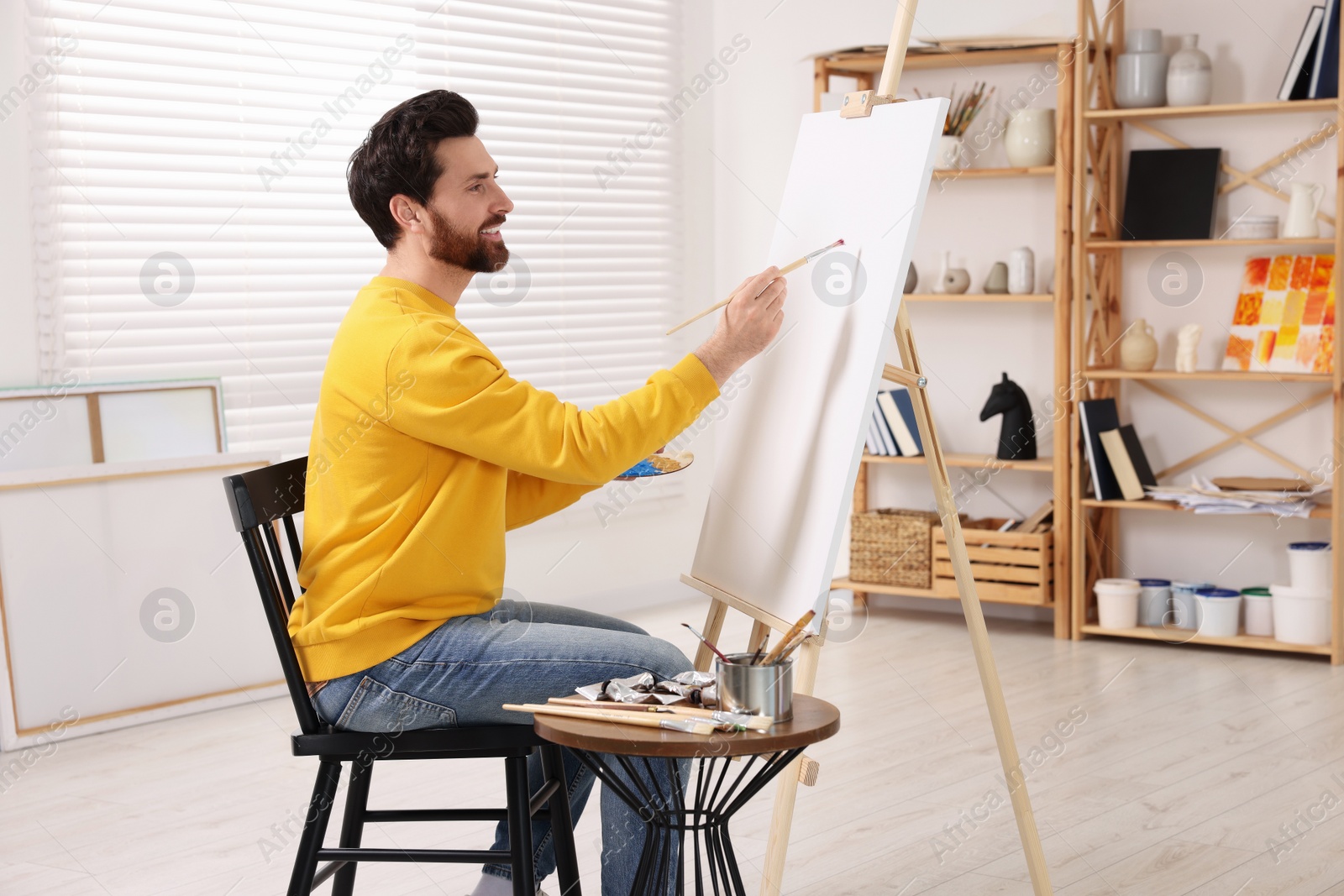 Photo of Man painting in studio. Using easel to hold canvas