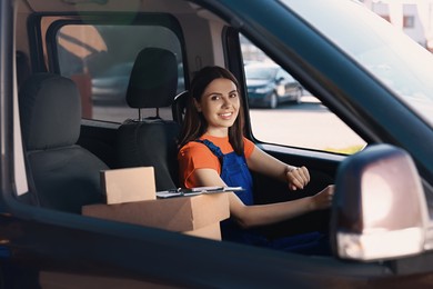 Photo of Courier with clipboard and parcels in car. Delivery service