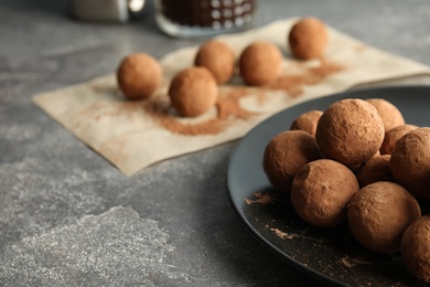 Photo of Plate with chocolate truffles on grey background, space for text