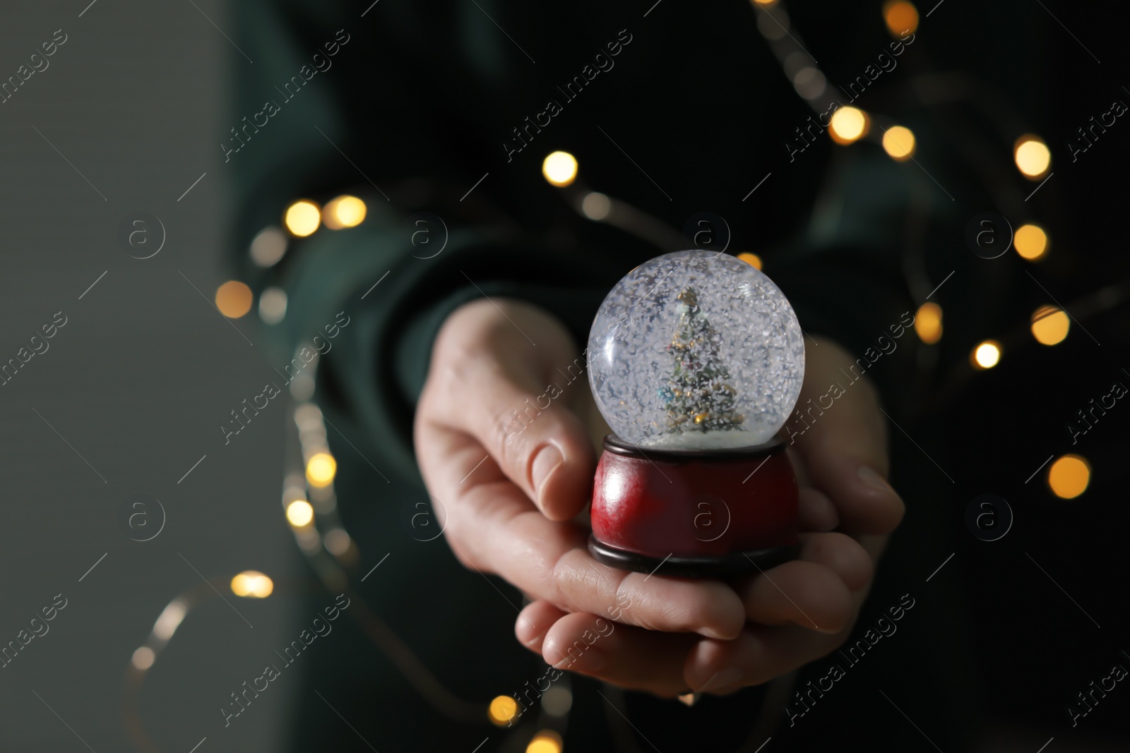 Photo of Woman holding Christmas snow globe on blurred background, closeup. Space for text