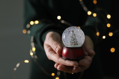 Woman holding Christmas snow globe on blurred background, closeup. Space for text