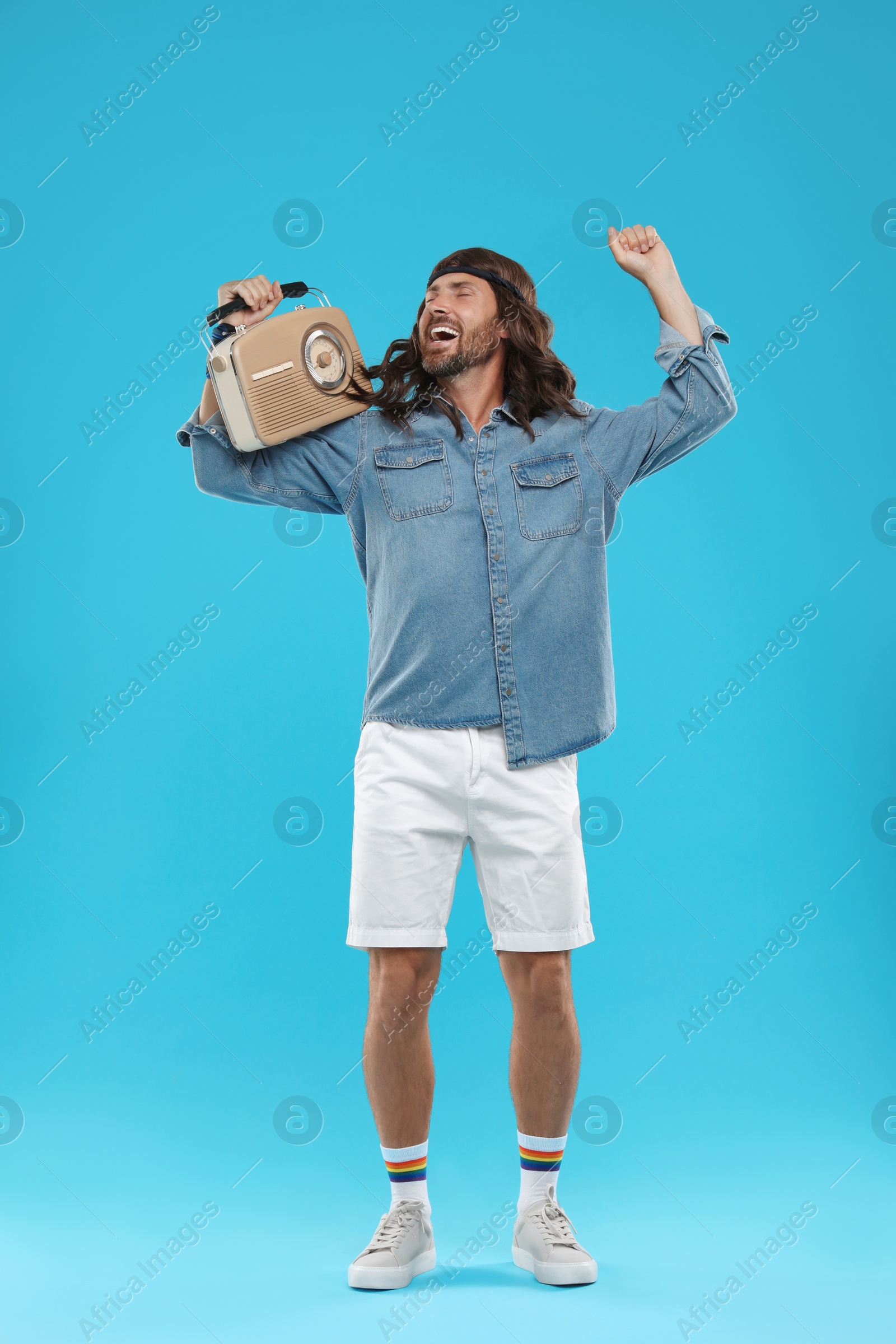 Photo of Stylish hippie man with retro radio receiver dancing on light blue background