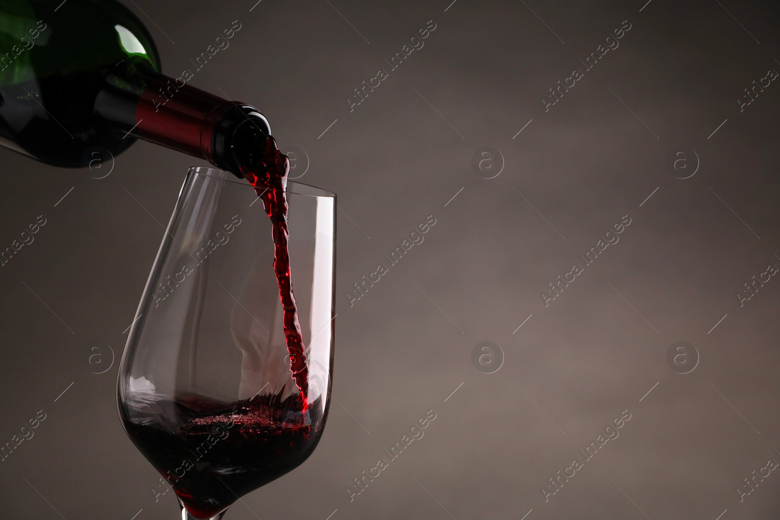 Photo of Pouring tasty red wine from bottle into glass on gray background, closeup. Space for text