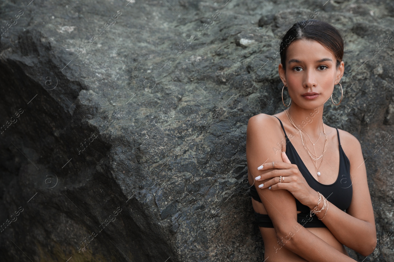 Photo of Beautiful young woman in stylish bikini near big stone outdoors, space for text