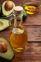 Glass bottle of cooking oil and fresh avocados on wooden table, closeup