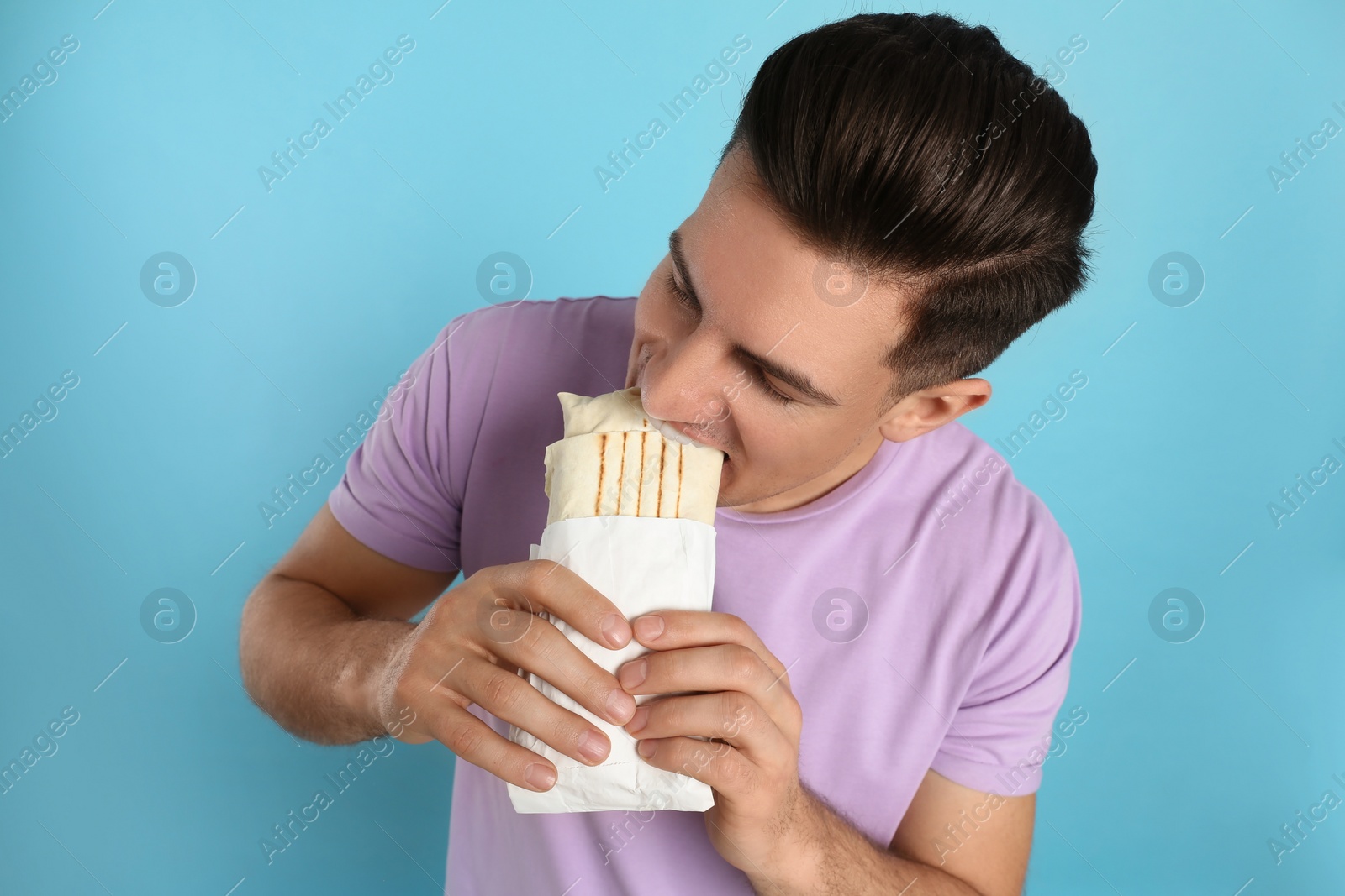 Photo of Man eating delicious shawarma on turquoise background