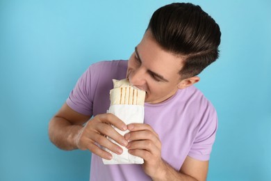 Man eating delicious shawarma on turquoise background