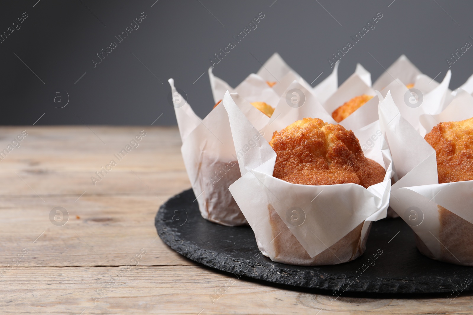 Photo of Delicious sweet muffins on wooden table against grey background, closeup. Space for text