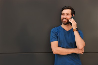 Photo of Happy man talking on phone near grey wall. Space for text