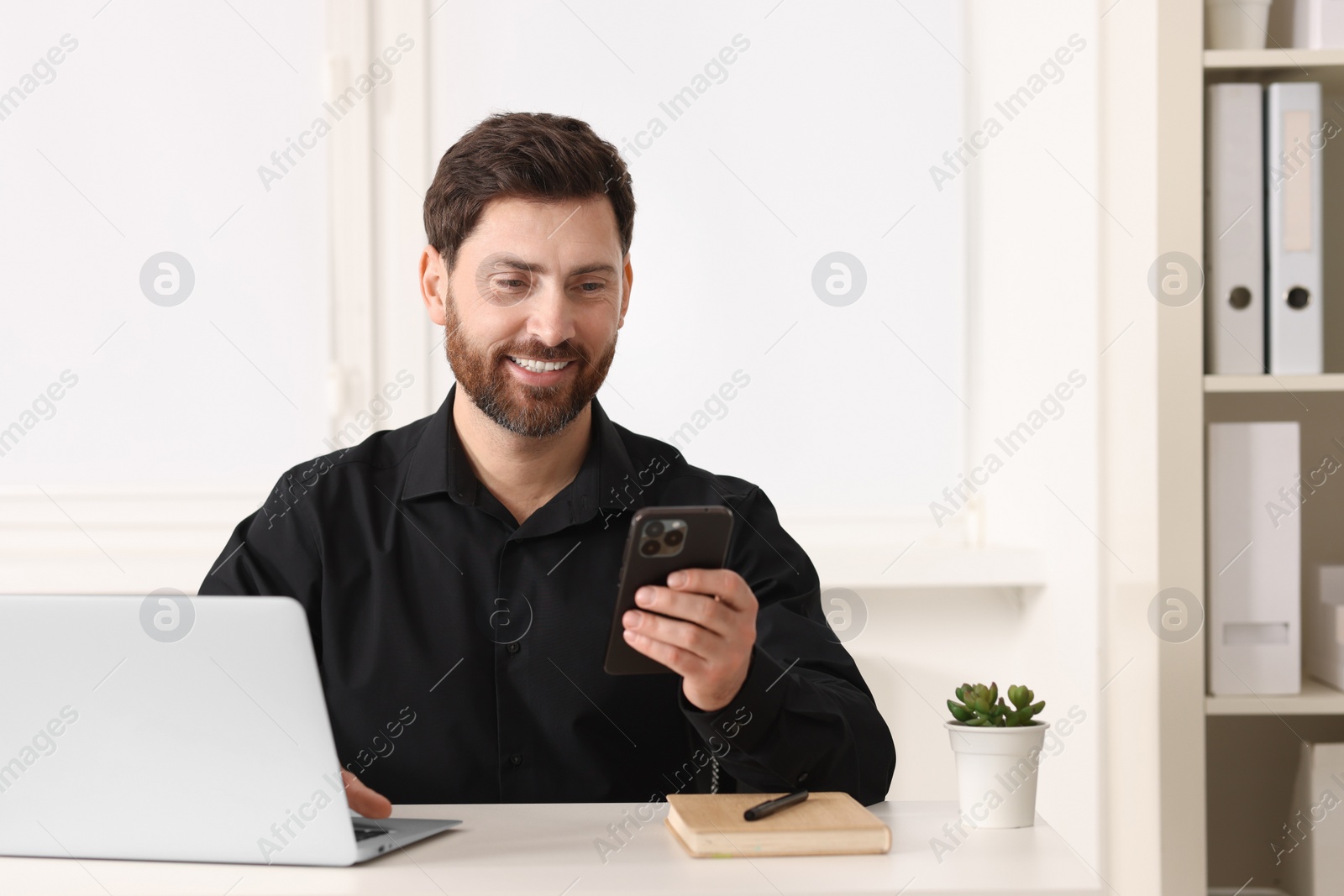 Photo of Smiling man using smartphone at table in office