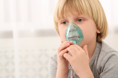 Sick little boy using nebulizer for inhalation indoors