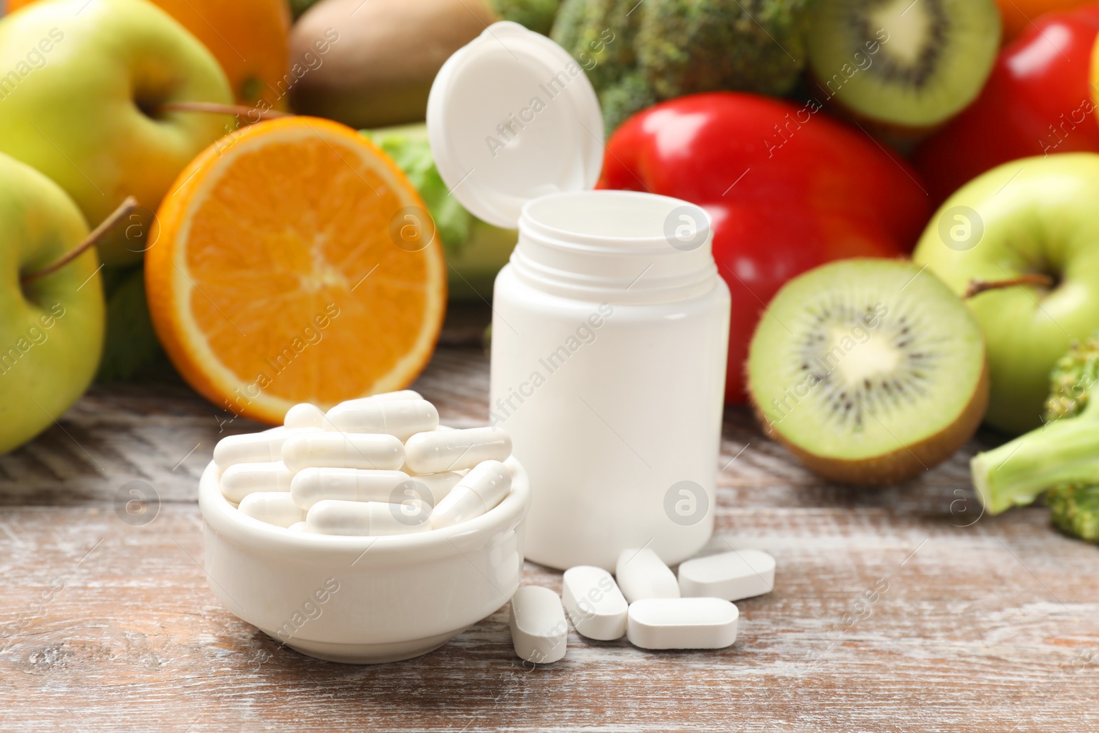 Photo of Dietary supplements. Plastic bottle, pills and food products on wooden table