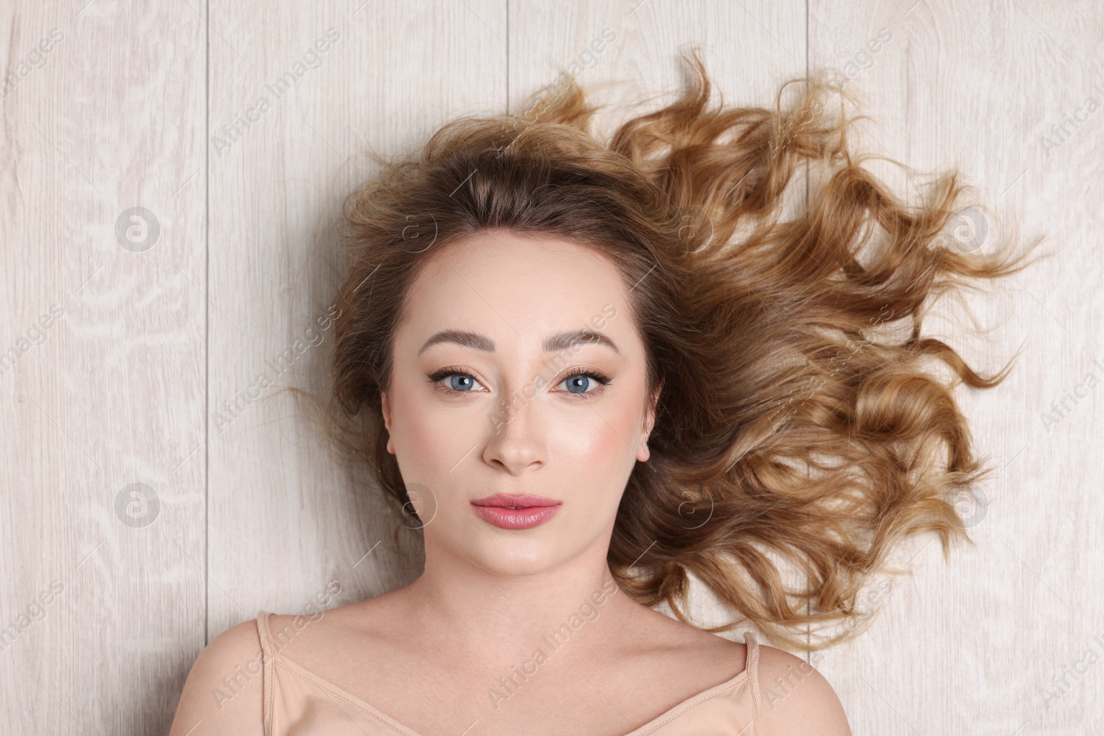 Photo of Portrait of beautiful woman with curly hair on wooden floor, top view