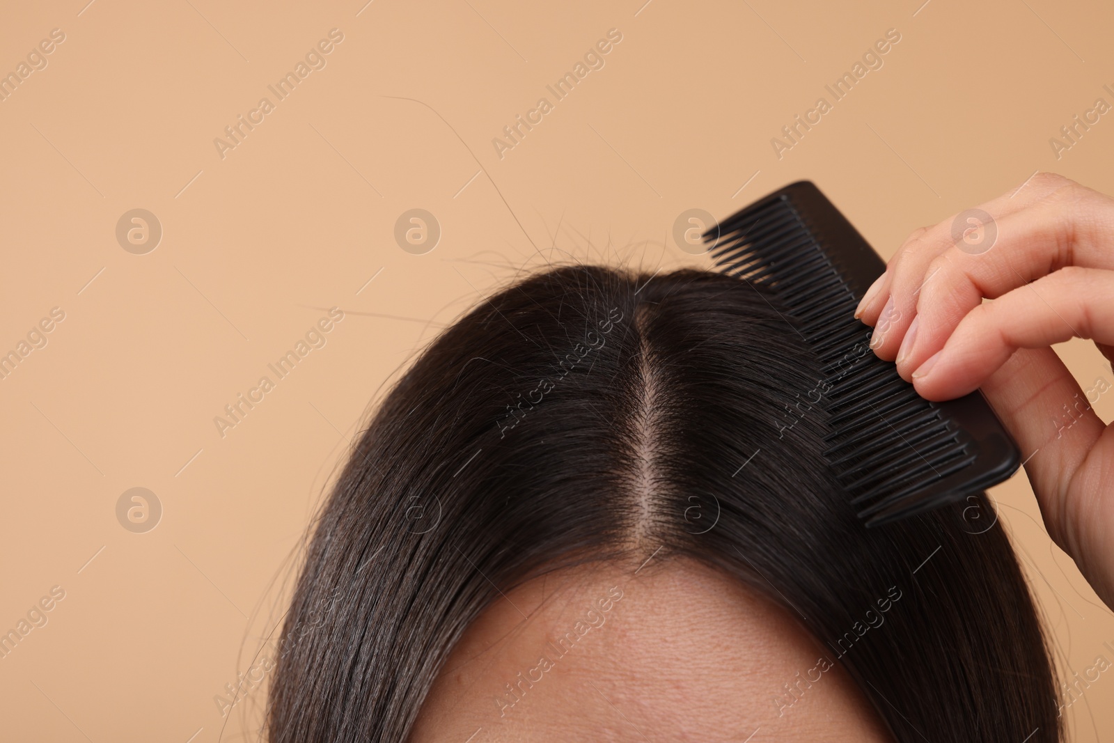 Photo of Woman with comb examining her hair and scalp on beige background, closeup