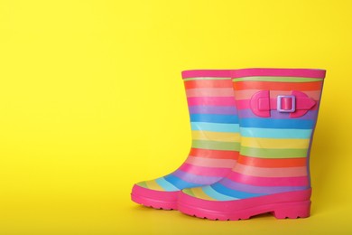 Photo of Pair of striped rubber boots on yellow background. Space for text