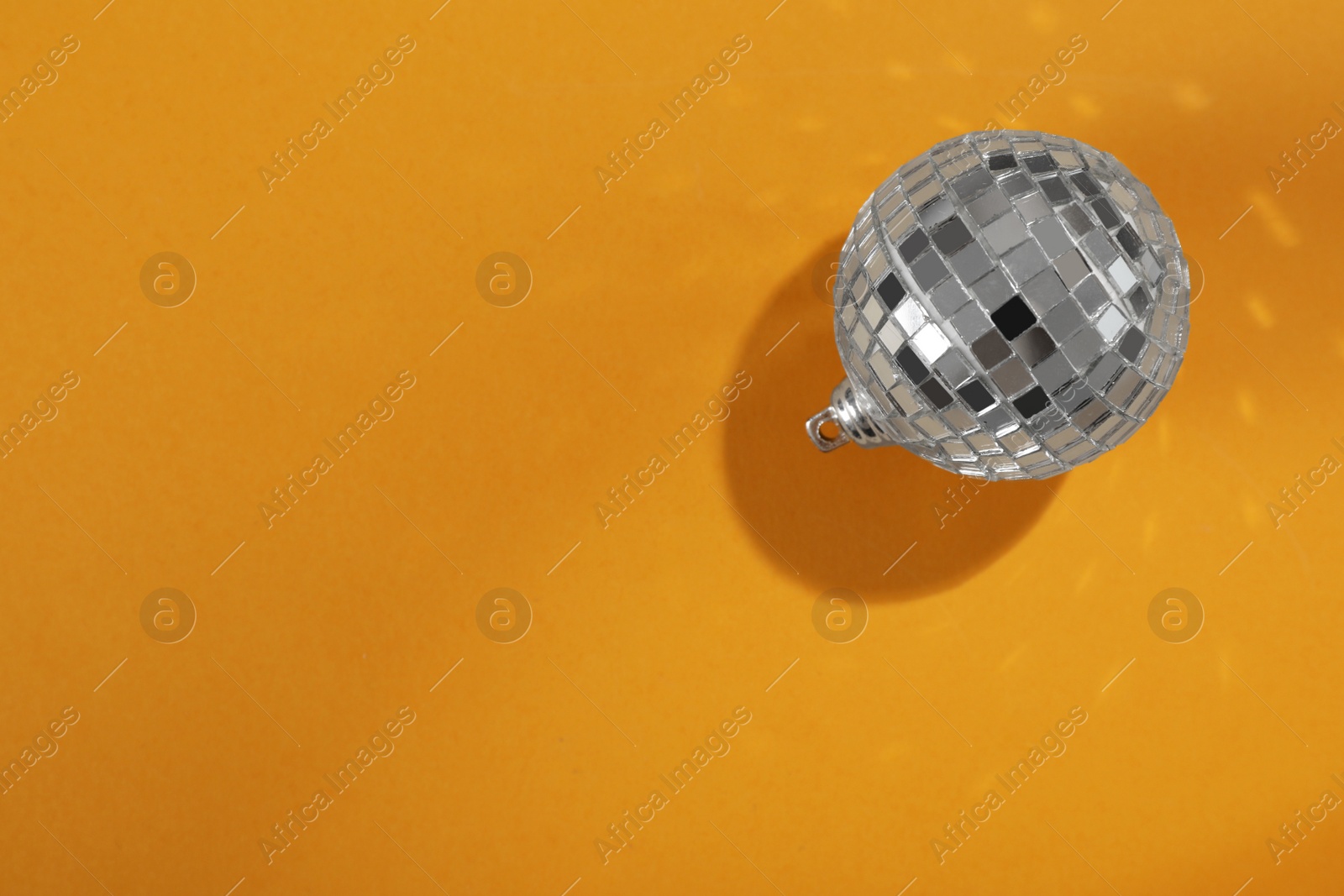 Photo of Bright shiny disco ball on orange background, top view. Space for text