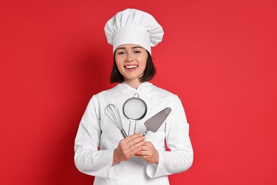 Photo of Happy confectioner holding professional tools on red background