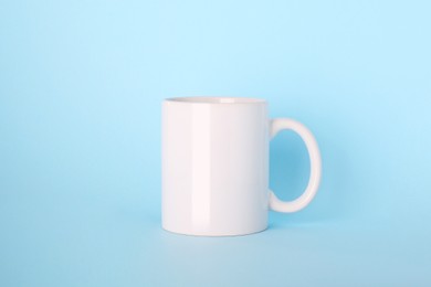 Photo of Blank white ceramic mug on light blue background