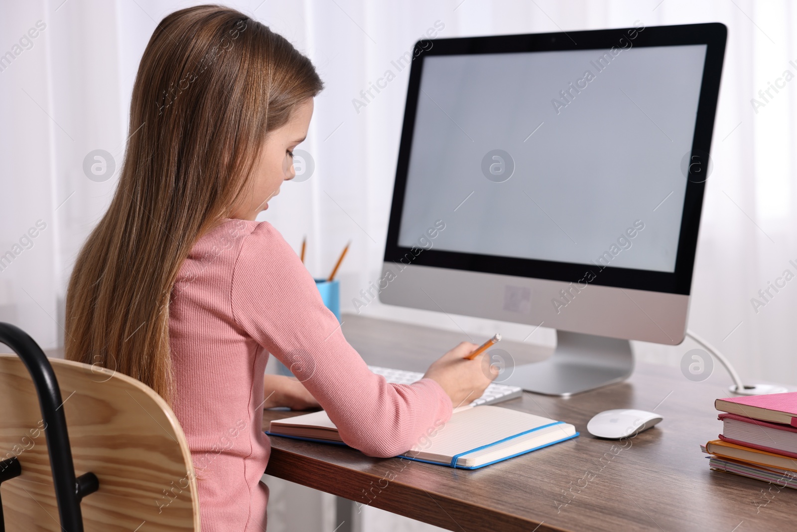 Photo of E-learning. Cute girl taking notes during online lesson at table indoors